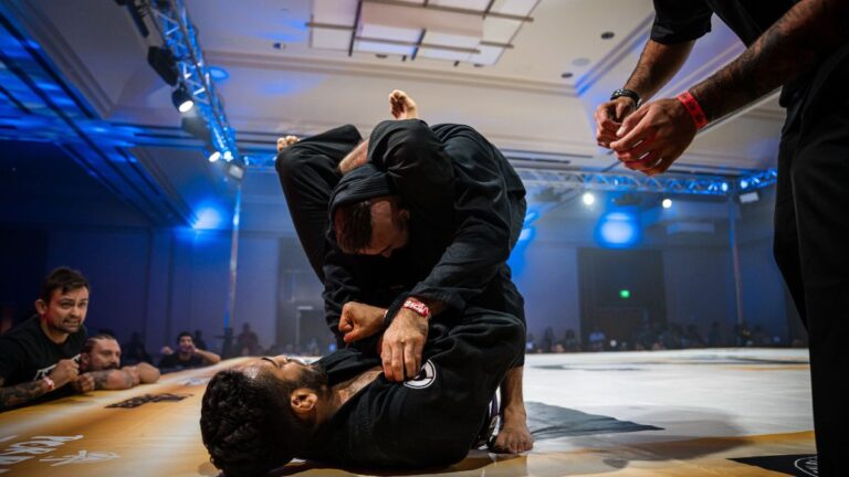 two bjj competitors sparring on a stage with head between legs